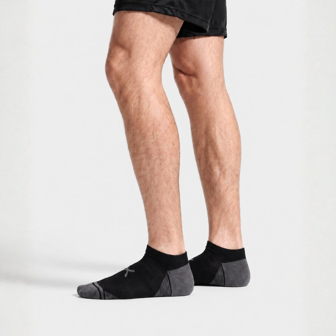 Black Power Stride Ankle Socks For Men in black with grey toe and heel, worn standing with black athletic shorts, side profile
