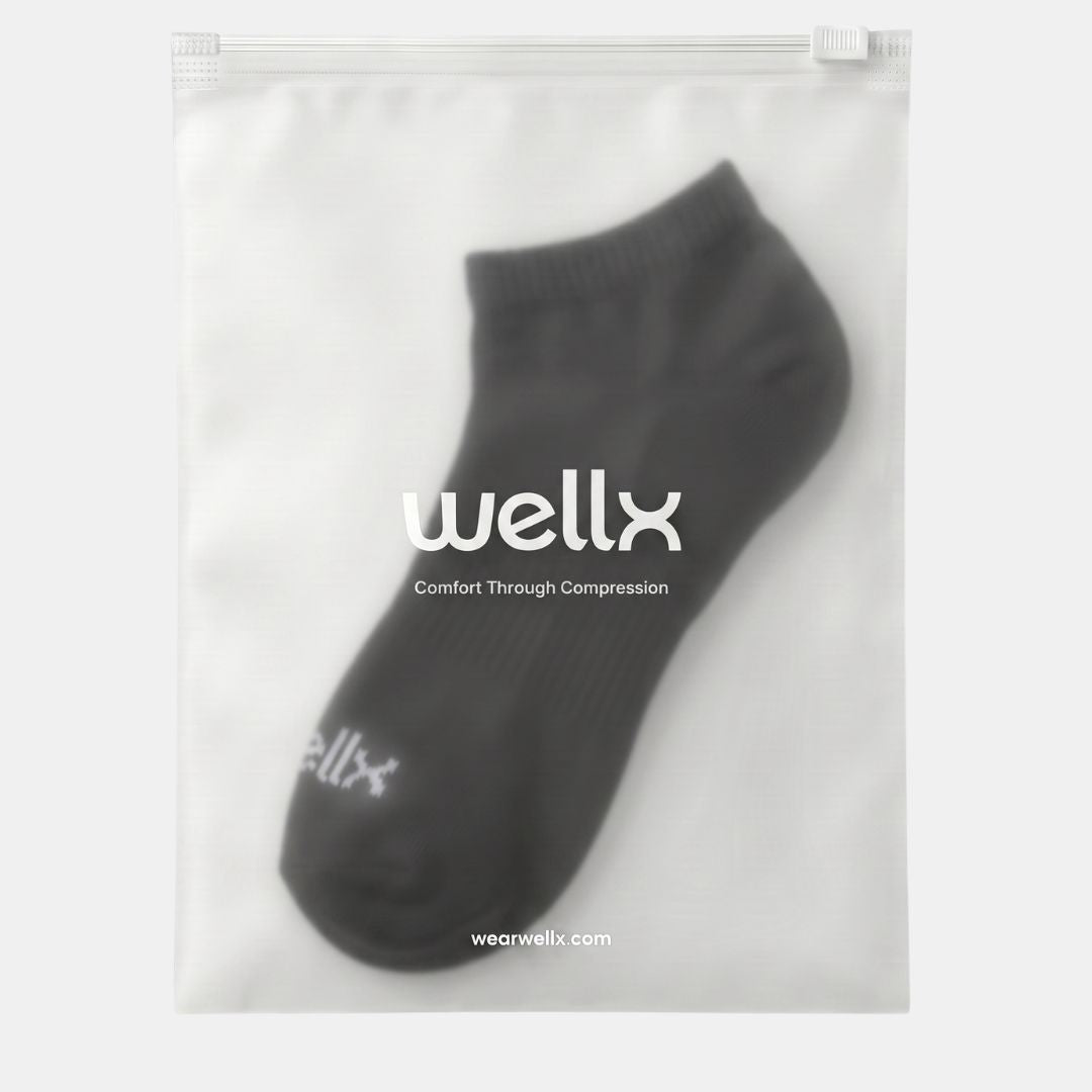Black Street Ankle Socks For Men. A single dark gray ankle sock displayed inside a clear zip-top pouch with white branding text reading 'wellx' and 'Comfort Through Compression' on a light gray background.