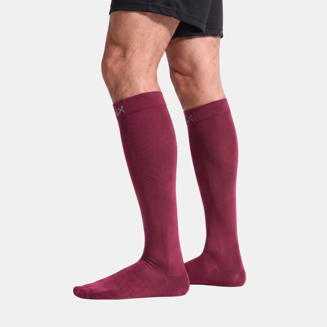 Burgundy Compression Socks For Men, A close-up of a person's legs and feet wearing Burgundy low-cut athletic socks against a clean white studio background.