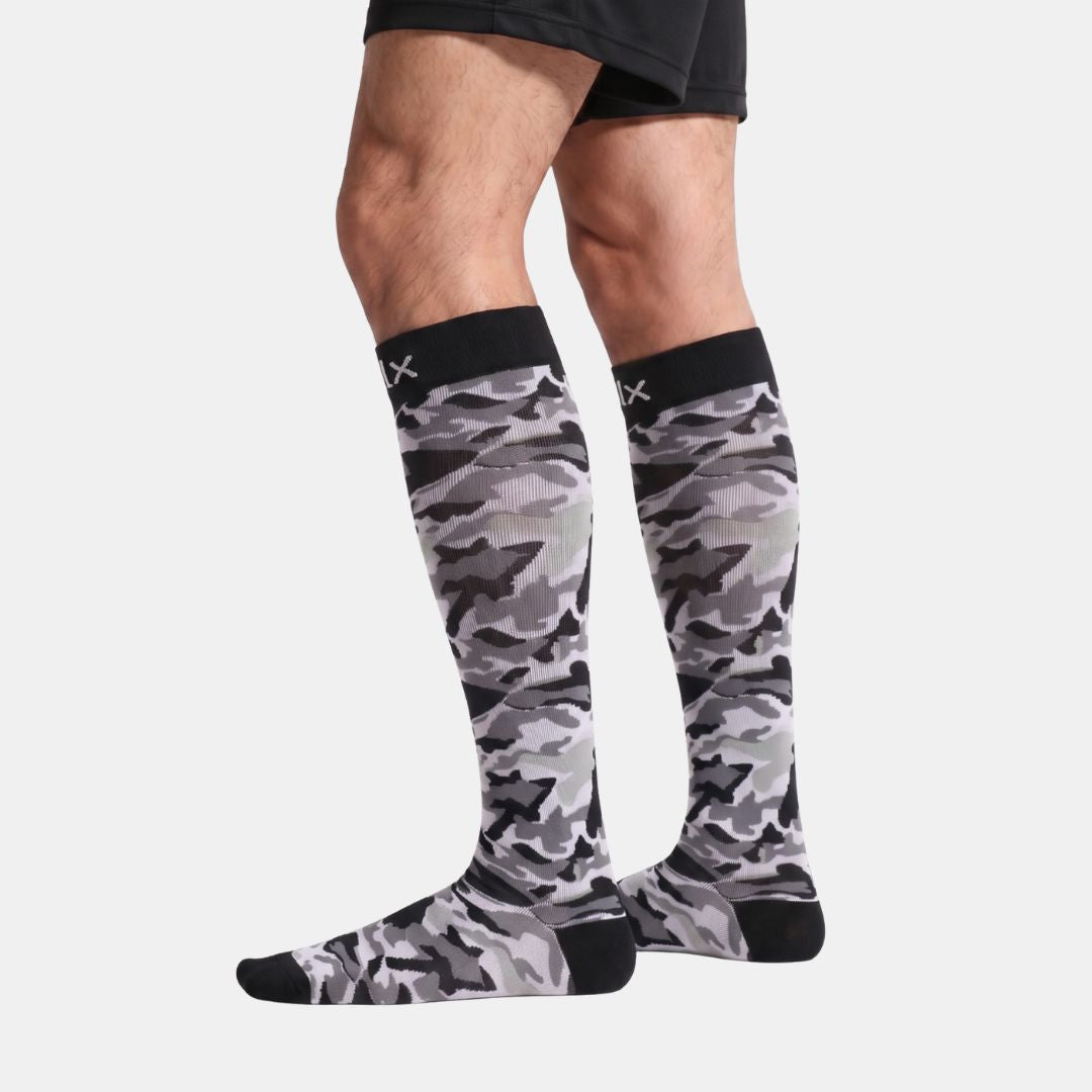 Stars Black Camouflage Compression Socks For Men displayed on a cropped male leg against a light gray background. The black camouflage-pattern ankle sock features highlighted benefits including a no-slip cuff, heel grip technology, targeted compression support, breathable fabric, anti-blister cushioning, and moisture-wicking sweat control for all-day comfort and performance.