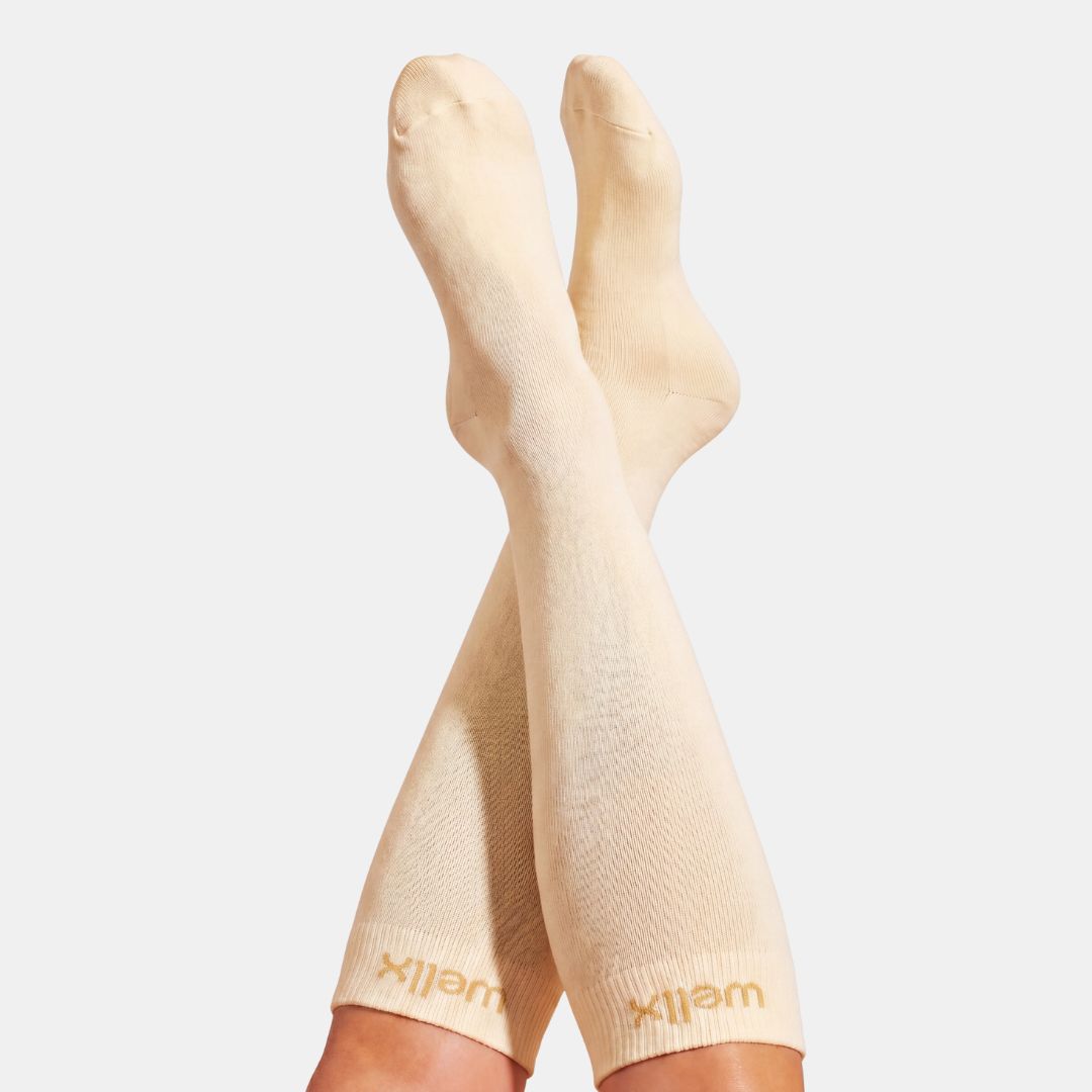 Candlelight Yellow Compression Socks For Men. A pair of beige compression socks worn on legs, shown against a light gray background. The brand name 'wellix' is printed in gold on the ribbed cuffs.