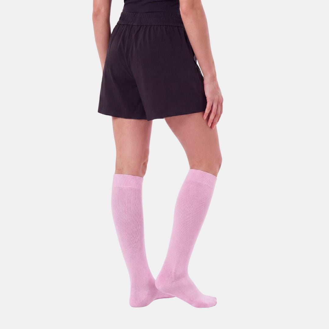 Candy Heart Pink Compression Socks For Women, A model from the waist down wearing pink knee-high socks with a small multicolor flower pattern, paired with dark shorts, against a light gray background.