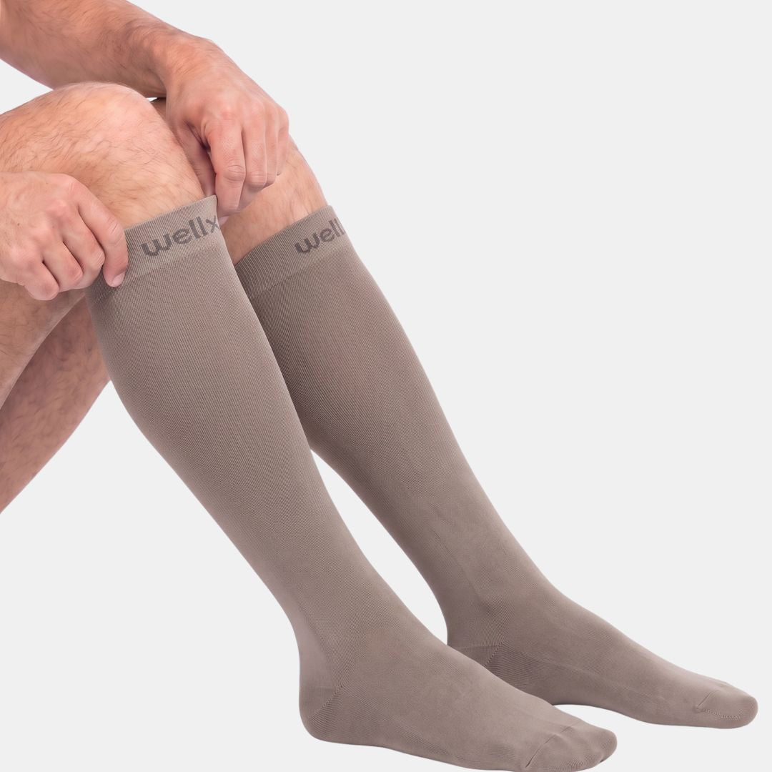 Gravel Compression Socks For Men,Taupe knee-high compression socks for men, shown being pulled up over the calf, side view on white background