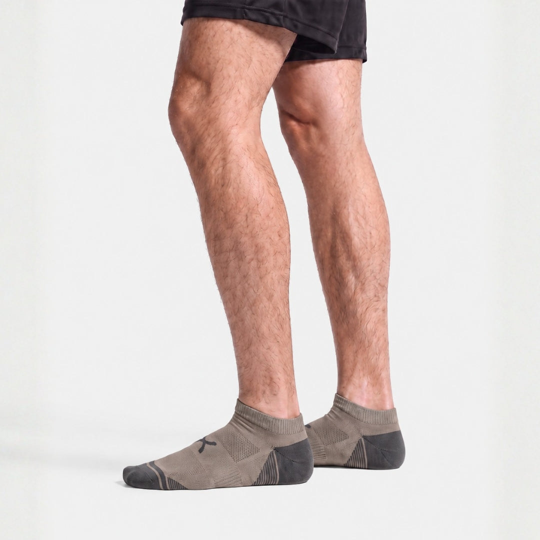 Gravel Power Stride Ankle Socks For Men in taupe with charcoal toe and heel, worn standing with black athletic shorts, side profile