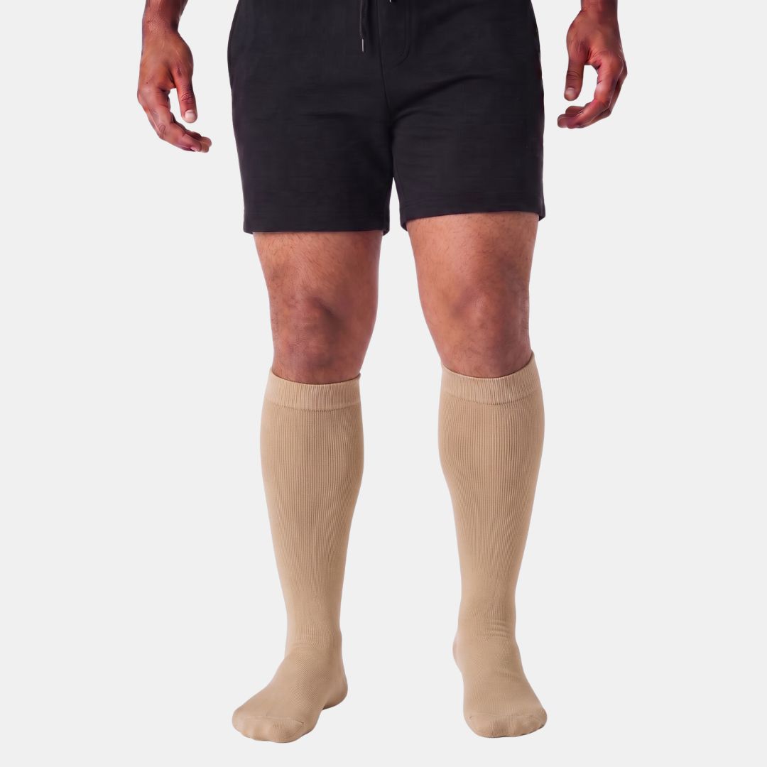 Light Brown Wide Calf Compression Socks For Men. A model from the waist down wearing black athletic shorts and beige knee-high compression socks against a light gray background.