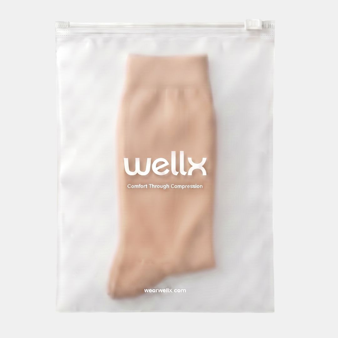 Light Brown Wide Calf Compression Socks For Men. A beige compression sleeve is neatly folded and displayed inside a clear, resealable plastic bag with the brand name 'wellx' printed in white on the front, set against a clean, light gray background.