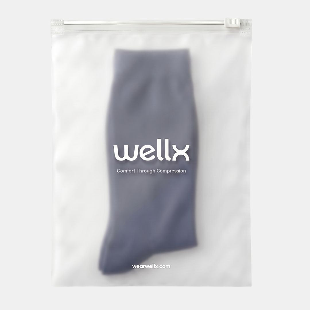 Navy Blue Wide Calf Compression Socks. A folded pair of gray compression socks inside a clear plastic resealable pouch with a white zipper, featuring the white 'wellx' logo and 'Comfort Through Compression' text on the front.
