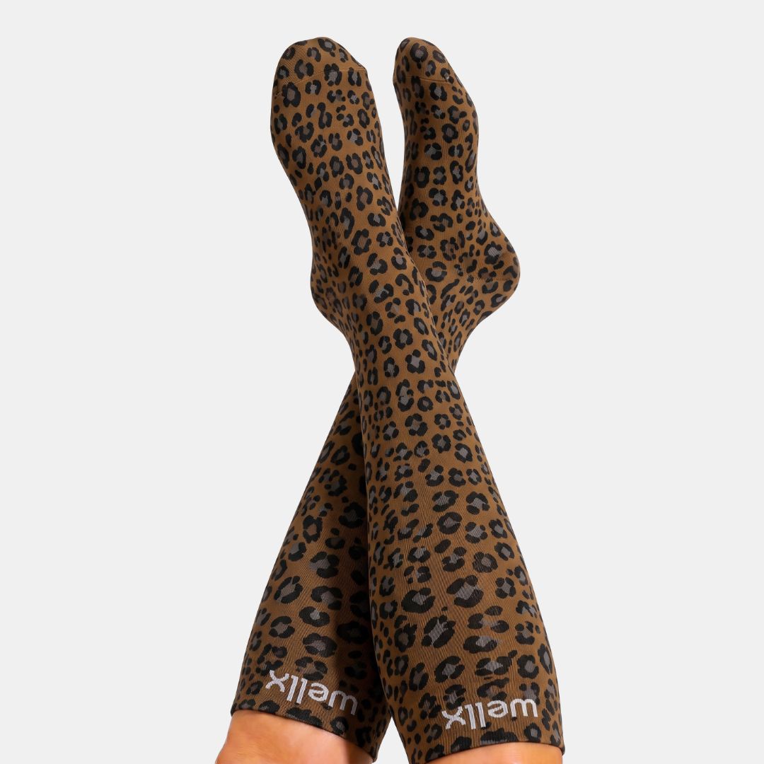 Panther Compression Socks For Women, A pair of leopard-print socks worn on legs, shown against a plain light gray background. The socks feature a brown and black leopard pattern with the brand name 'wellix' printed in white near the cuffs.