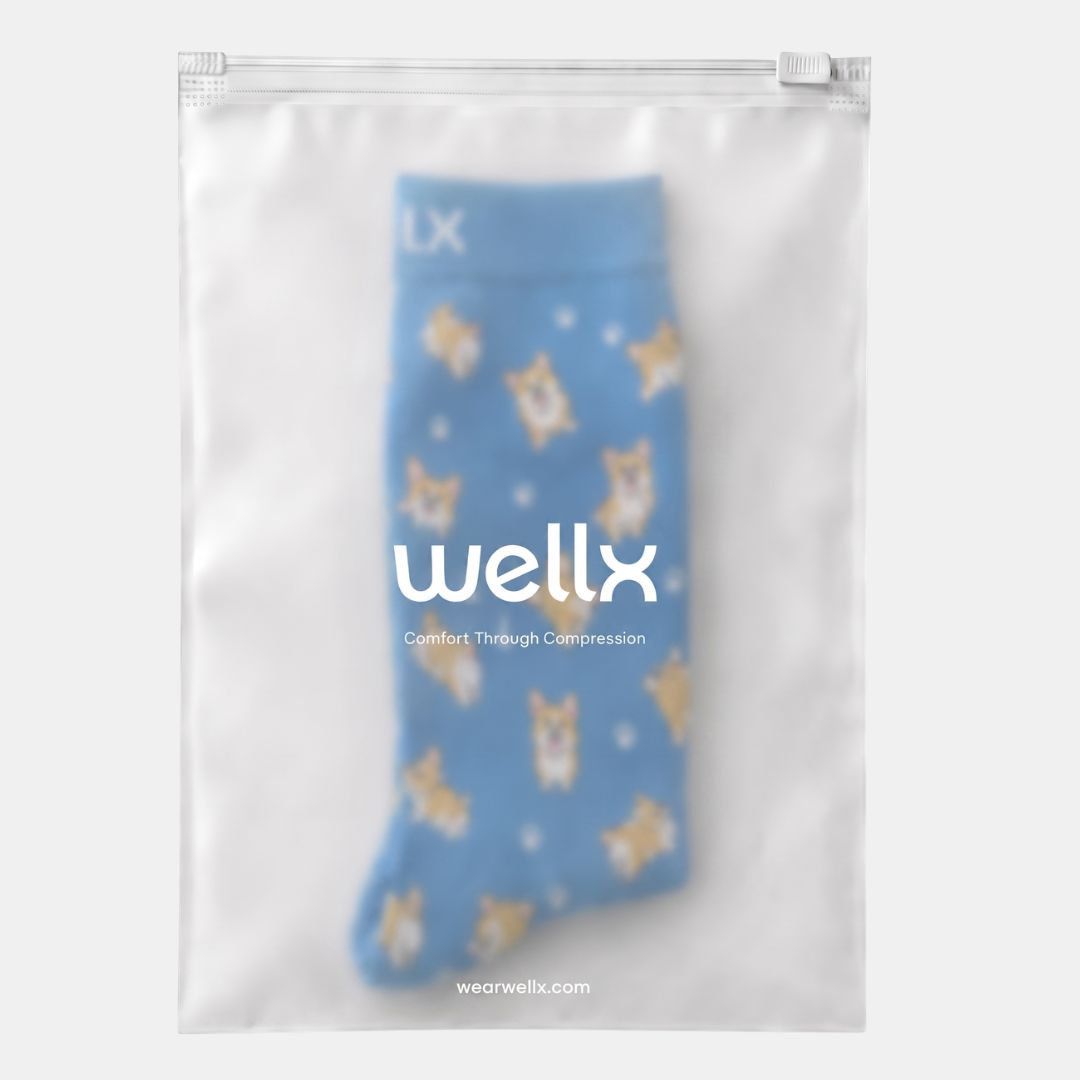 Puppies Blue Compression Socks For Men, A blue compression sock with a yellow dog pattern, packaged inside a clear zippered plastic sleeve with the brand name 'wellx' printed on the front.