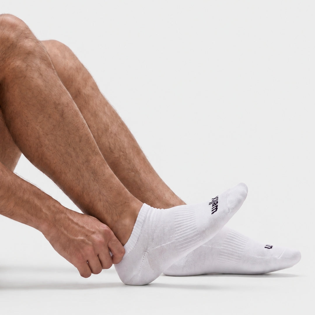 White Street Ankle Socks For men A close-up of a person's legs and hand adjusting white ankle socks against a clean light gray studio background.