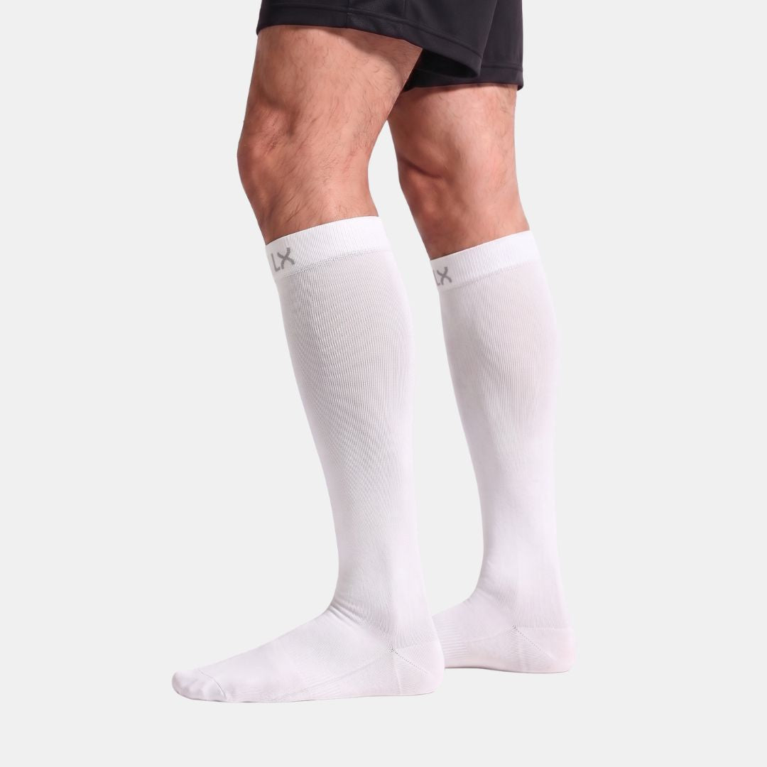 Compression Socks For Men, White knee-high compression socks worn on a model's legs, shown against a light gray studio background with black athletic shorts partially visible at the top.