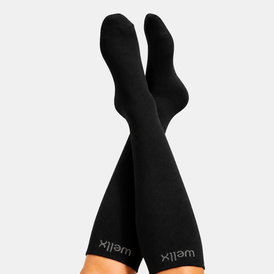 Black Compression Socks for Men, Black compression socks worn on crossed legs, with the brand name 'wellix' visible near the cuffs, against a light gray background.