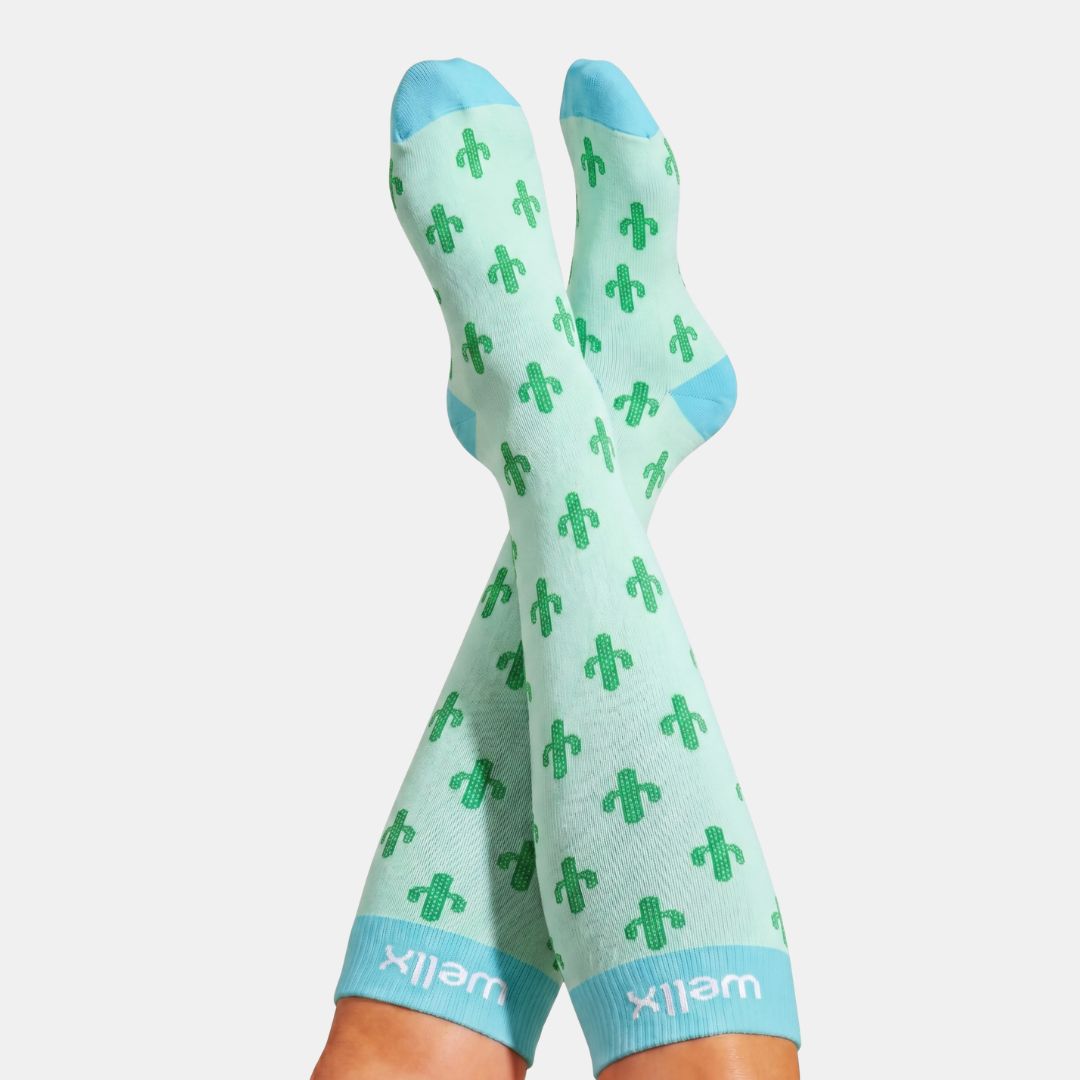 Cactus Green Compression Socks For Men, A pair of mint green crew socks with a green cactus pattern and light blue toes, heels, and cuffs, worn on legs against a light gray background.