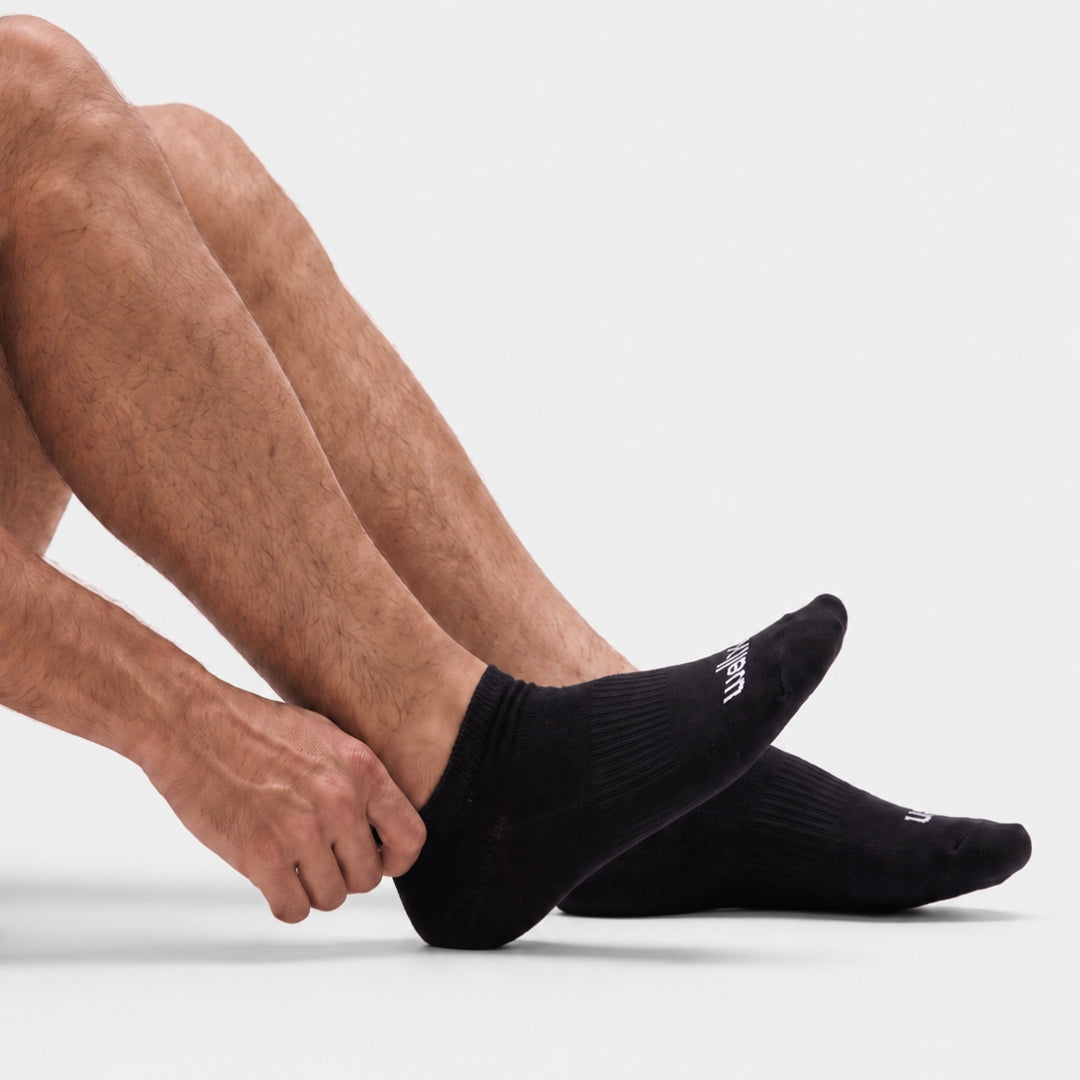 Black Street Ankle Socks For Men. A close-up of a person's legs and feet wearing black low-cut athletic socks against a clean white studio background.