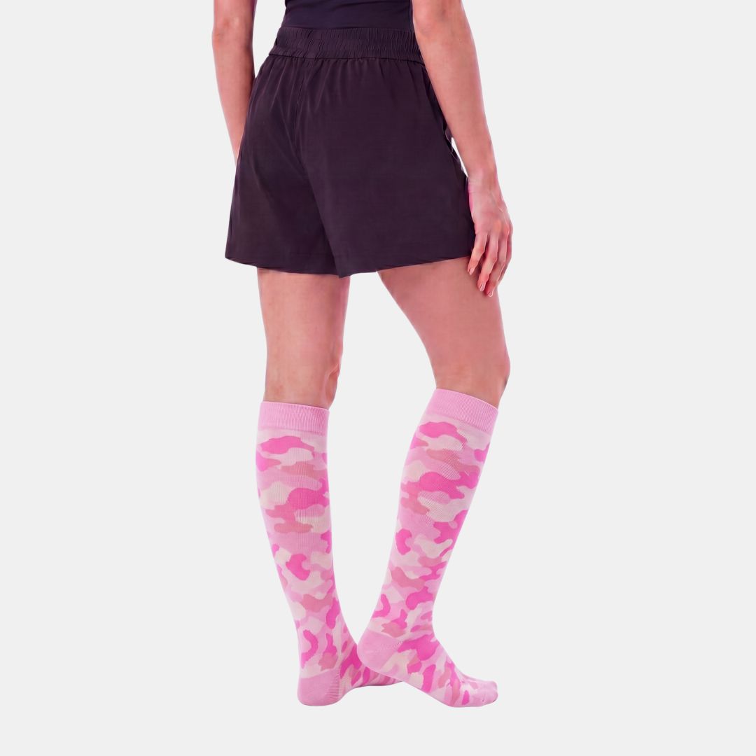 Camouflage Pink Compression Socks For Women, A model from the waist down wearing pink and light pink camouflage knee-high socks with dark shorts, shown against a light gray background.