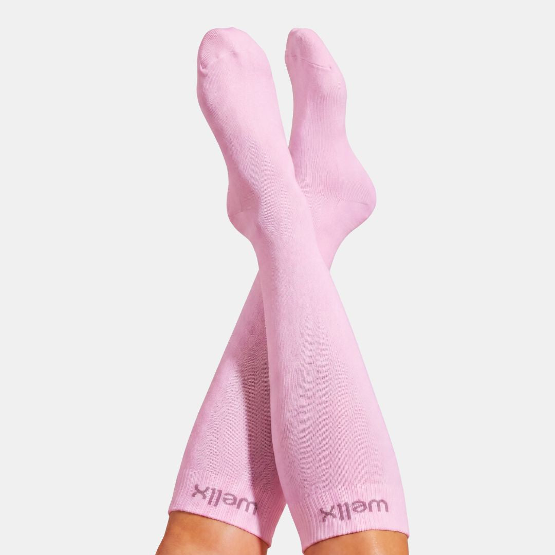 Candy Heart Pink Compression Socks For Women, A pair of light pink crew socks worn on crossed legs, with the brand name 'wellix' visible near the cuffs, against a light gray background.