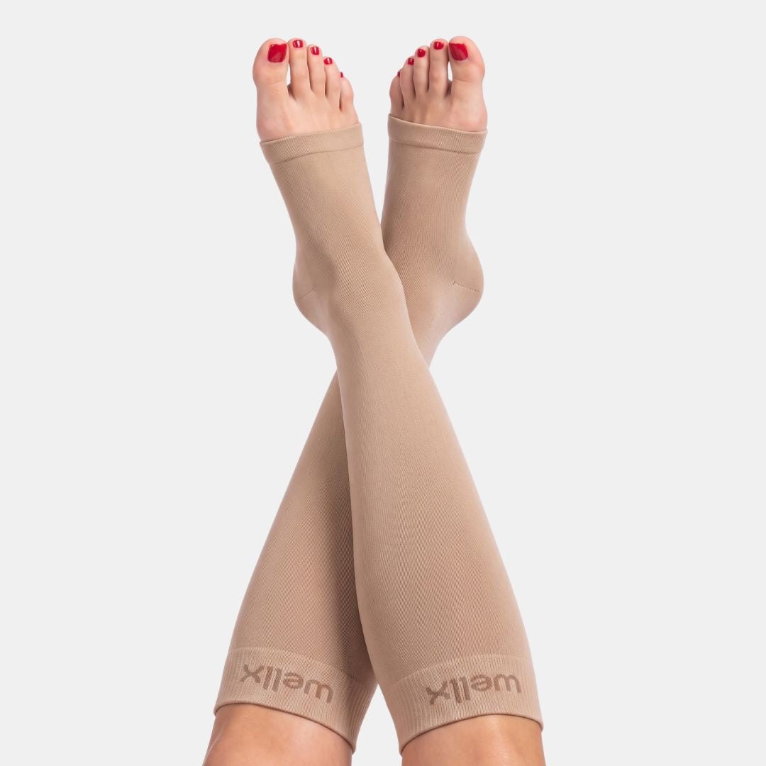 Gravel Toeless Compression Socks For women Beige calf compression sleeves worn on a person's legs, shown against a light gray background. The brand name 'wellx' is visible on the cuffs.