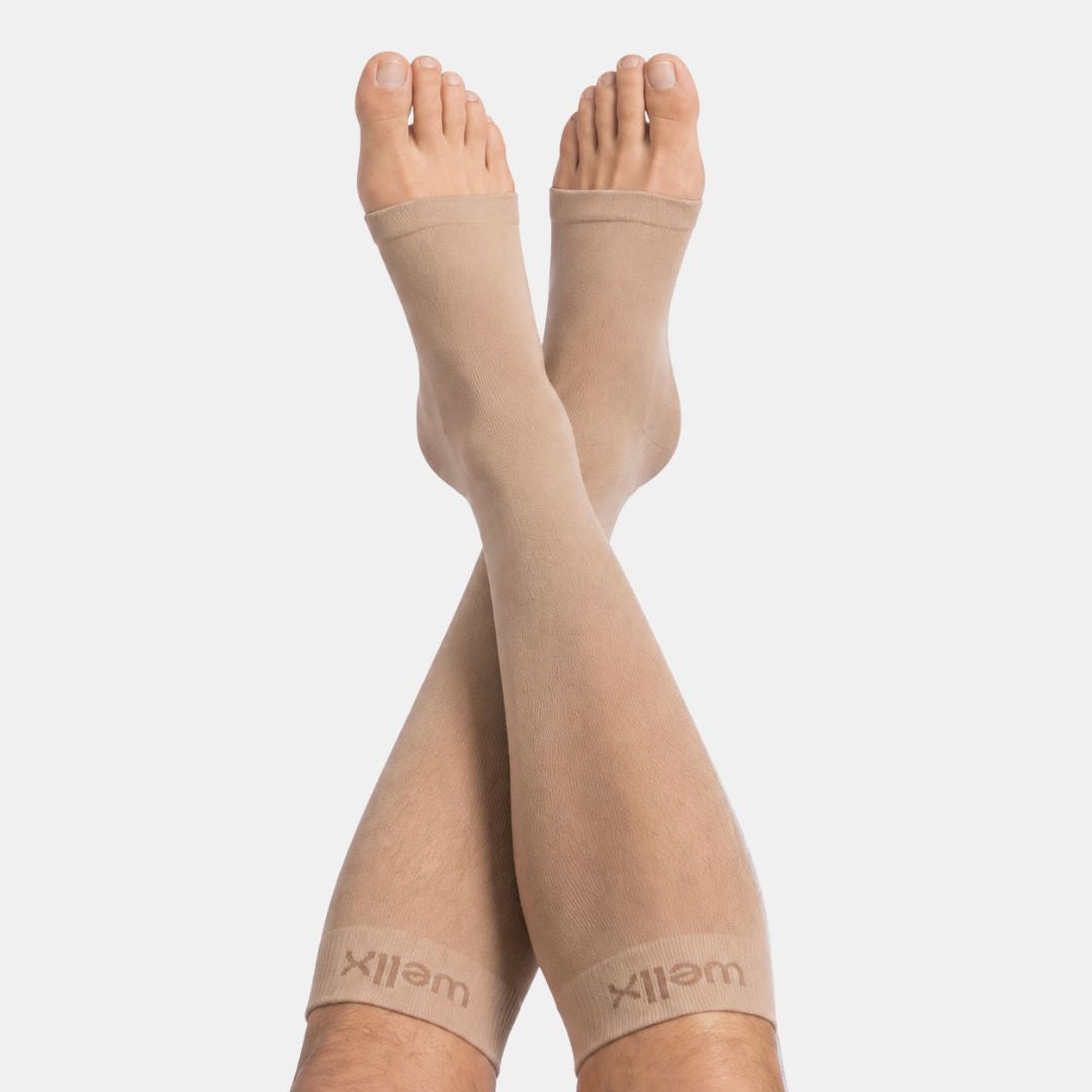 Gravel Toeless Compression Socks For Men  A pair of beige compression socks worn on crossed legs, shown against a plain light gray background. The brand name 'wellX' is visible on the cuffs.