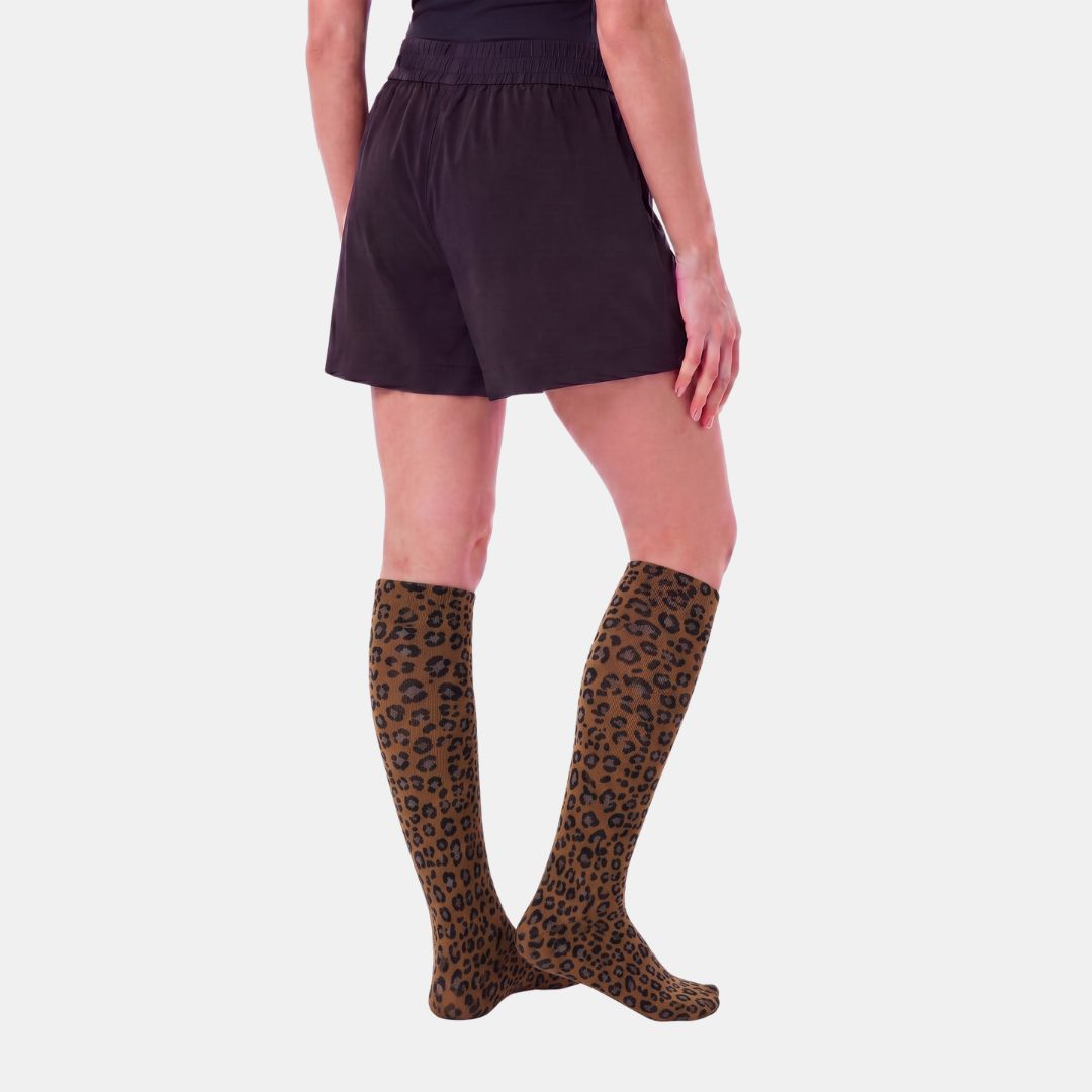Panther Compression Socks For Women, A model from the back wearing brown and black leopard-print knee-high socks with dark shorts, set against a light gray background.