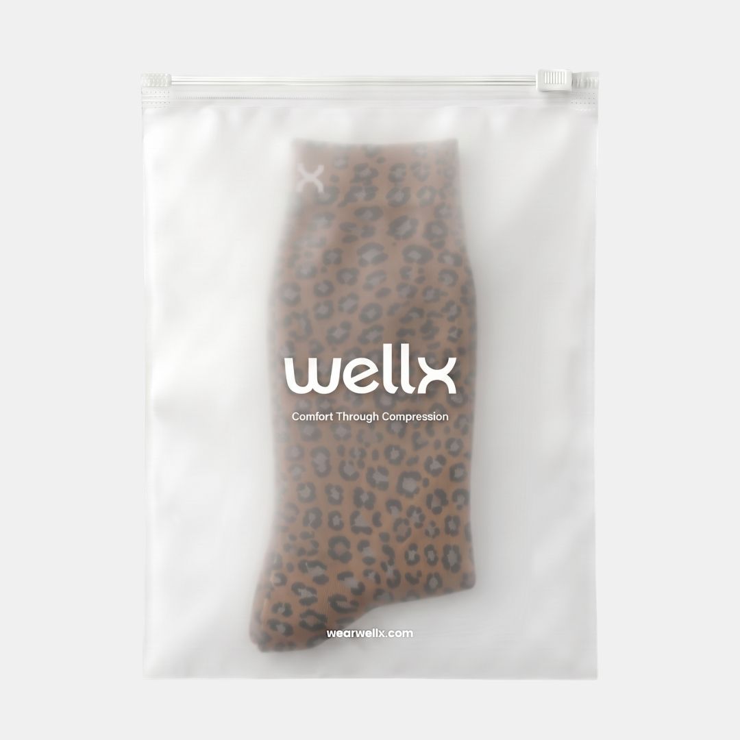 Panther Compression Socks For Women, A pair of brown leopard-print compression socks inside a clear, zippered plastic storage bag with the brand name 'wellx' printed on the front, set against a plain light gray background.