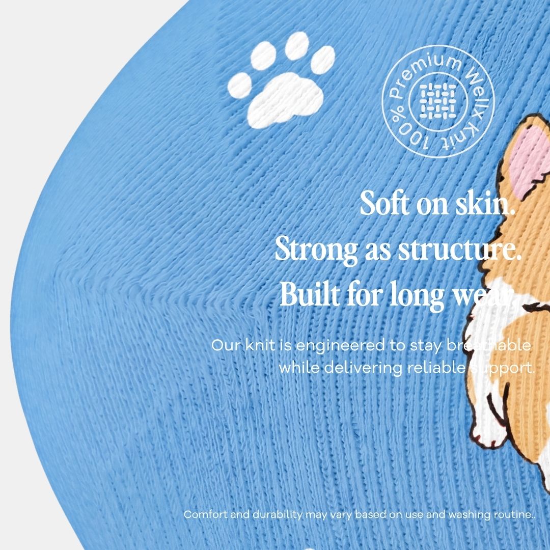 Puppies Blue Compression Socks For Men,  Close-up of a light blue knit pet accessory, likely a sweater or blanket, with a white paw print, a circular '100% Premium Wool Knit' badge, and text describing softness and durability. Part of a tan and pink dog illustration is visible on the right edge.